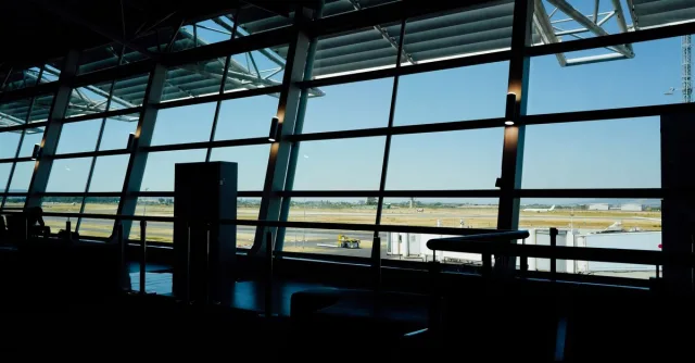 View from inside an airport terminal overlooking the runway under a bright blue sky.