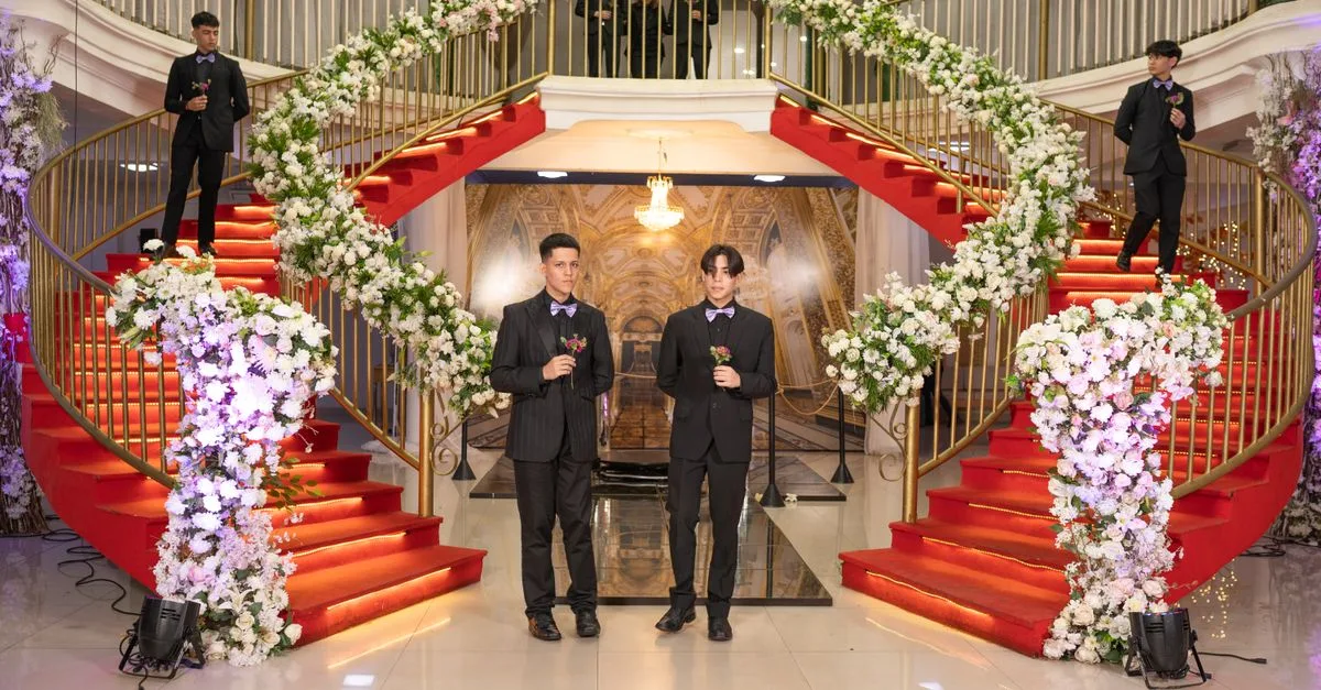 Formal occasion with men in suits, surrounded by floral decorations on a grand red staircase.