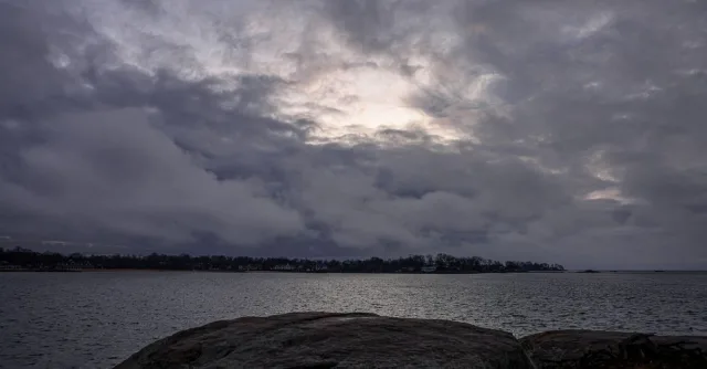 A dramatic seascape with dark clouds and a rocky shore captured at twilight, conveying a moody atmosphere.