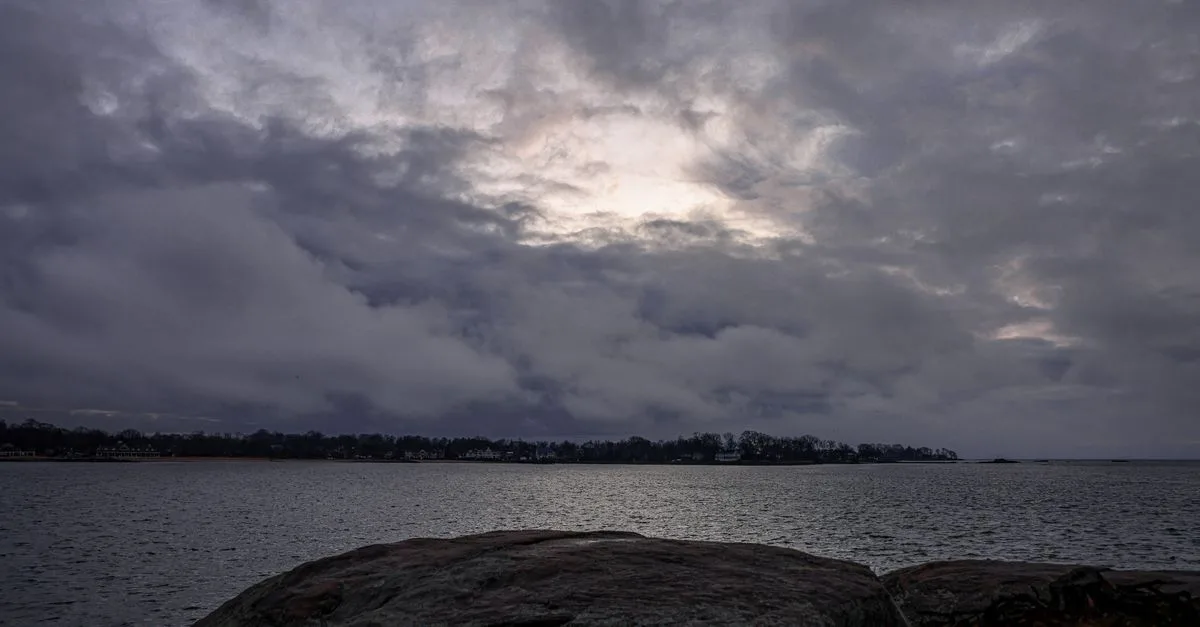 A dramatic seascape with dark clouds and a rocky shore captured at twilight, conveying a moody atmosphere.