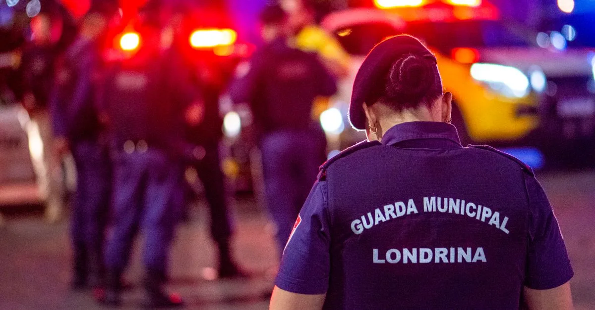 A municipal guard stands on duty in the vibrant streets of Londrina at night.