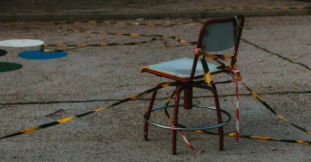 An empty metal chair wrapped with barricade tape on an outdoor paved surface.