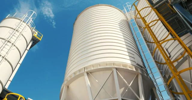 Wide-angle view of industrial silos with clear blue sky, captured during daytime, showcasing modern industry.