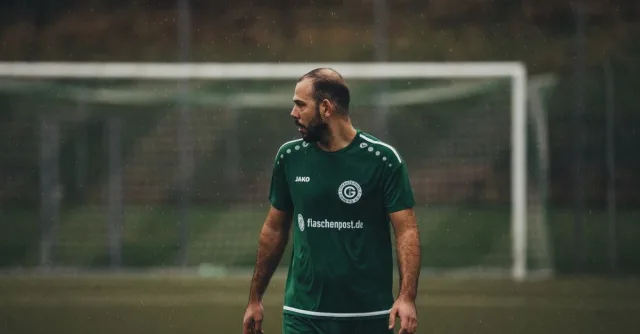 Soccer player in green uniform on a wet field during a rainy day match.