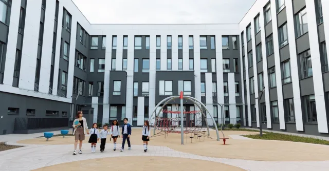 Group of students and teacher walking in a school courtyard with modern architecture and playground.