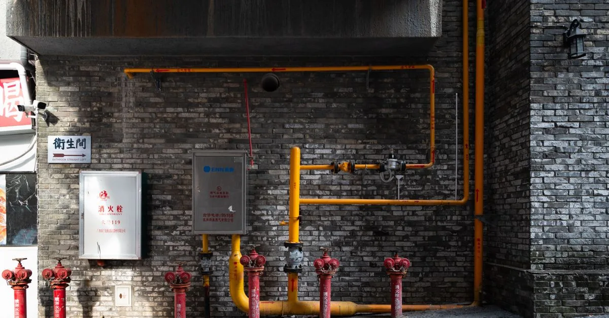 Brick wall with red hydrants and yellow piping in an urban alleyway setting.