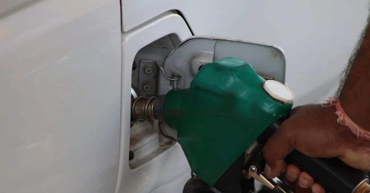 Close-up of a hand refilling a car's gas tank at a station with a green fuel nozzle.