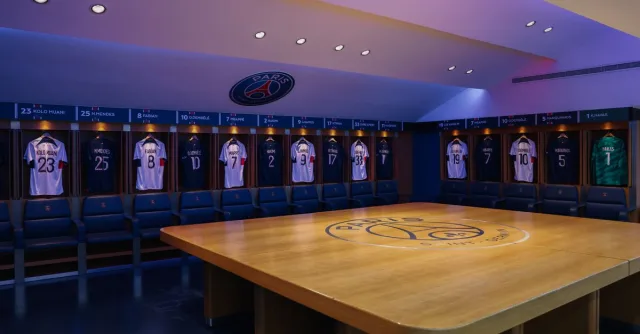 Interior view of Paris Saint-Germain's locker room featuring team jerseys and emblem.