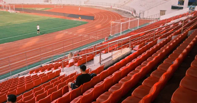 Quiet football stadium in Hải Phòng, Vietnam, with red seats and a lush green field.