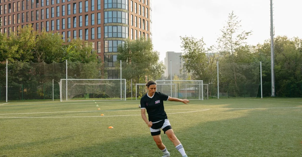 A woman practicing soccer skills on a city field with tall buildings in the background.
