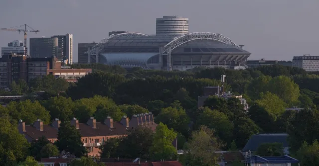 A modern cityscape of Amsterdam featuring the iconic football stadium amidst urban and green areas.
