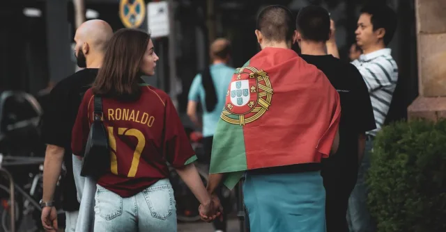 A group of football fans in Berlin, one wearing a Portugal flag, walking the street.