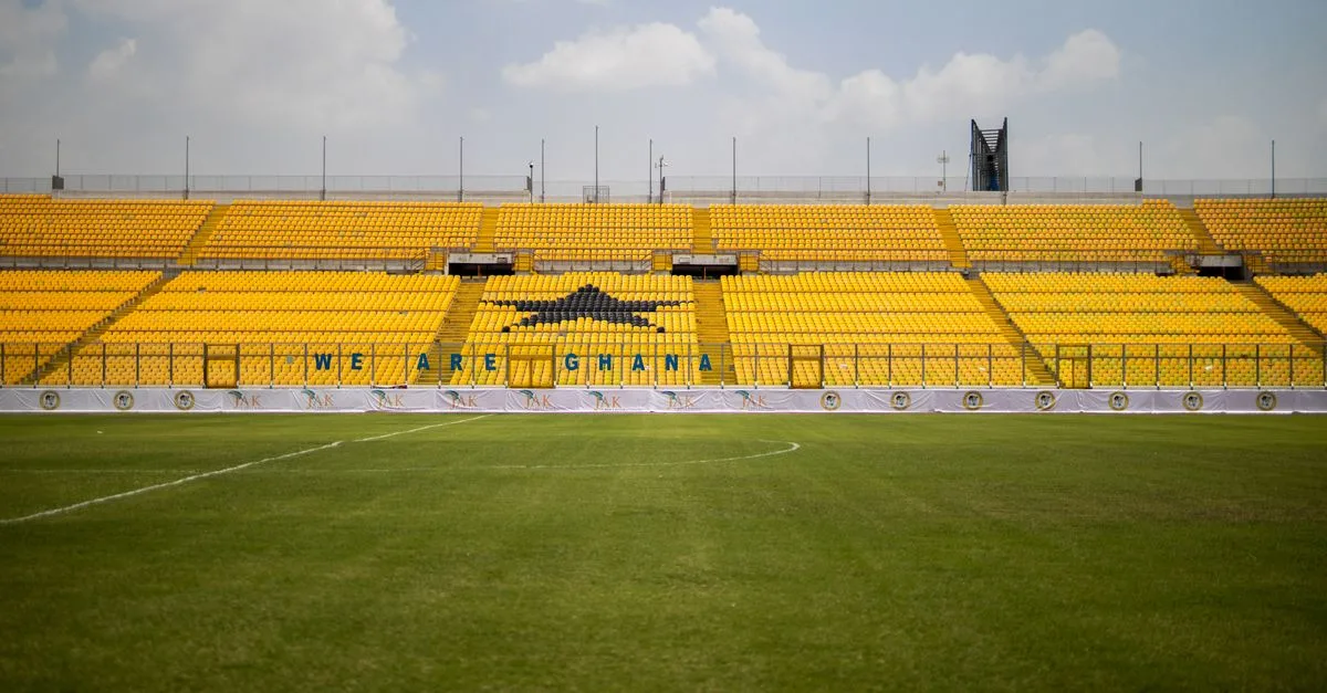 Stadium with bright yellow seats and green lawn under a blue sky in Ghana. Ideal for sports events.