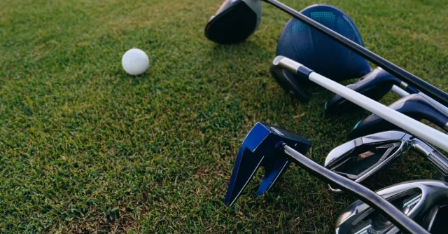 A close-up view of golf clubs and a golf ball on a lush green grass field.