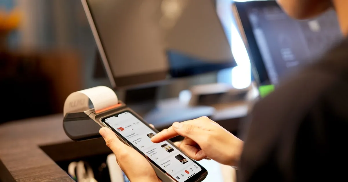 A person using a smartphone for payment at a modern POS terminal indoors.
