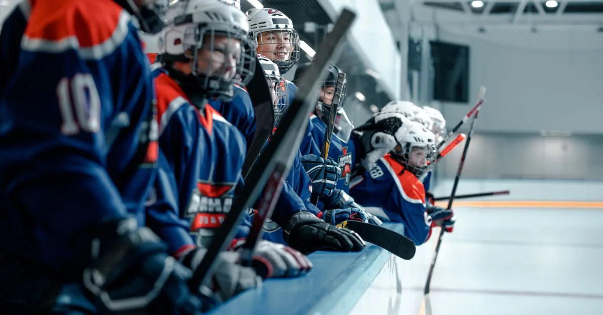 A youth ice hockey team wearing blue jerseys and helmets stands ready on the rink.
