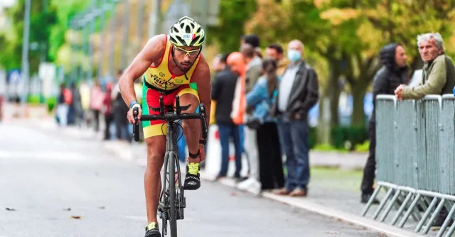 Cyclist in vibrant gear racing outdoors with spectators watching.