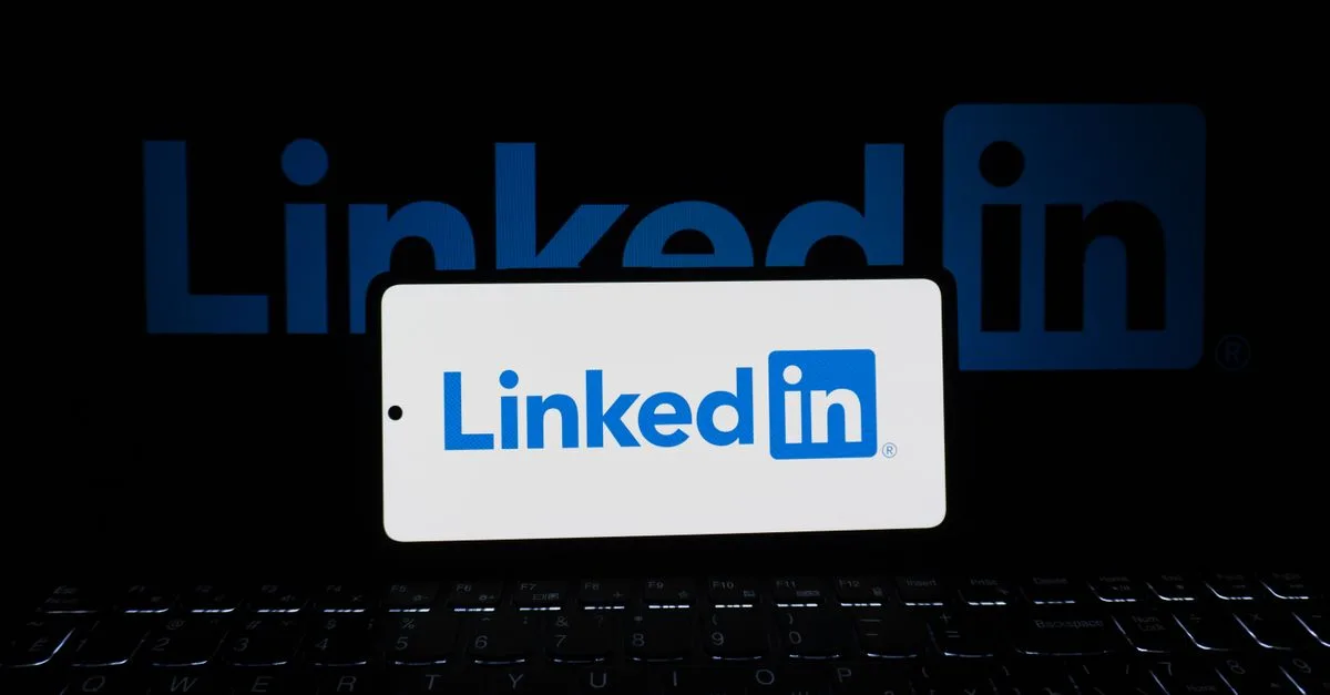 Smartphone showing LinkedIn logo with keyboard and large background logo, business theme.