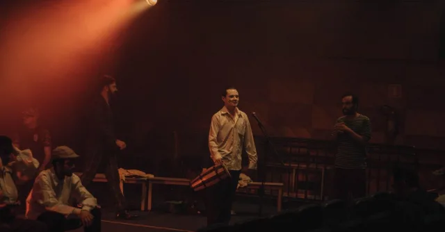 Actors in a dimly lit theater rehearsing under warm stage lights.
