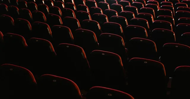 Rows of empty red seats in a dimly lit theater, creating a moody atmosphere.