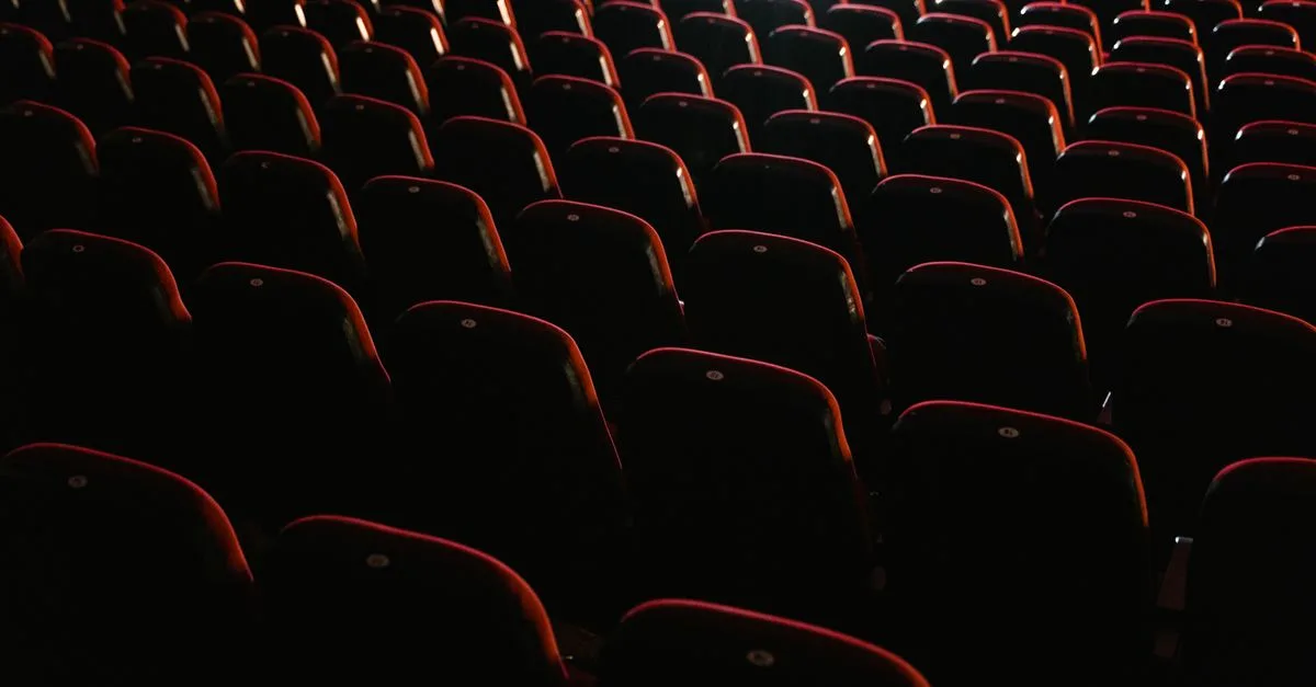 Rows of empty red seats in a dimly lit theater, creating a moody atmosphere.