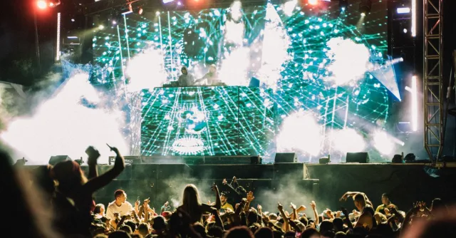 Vibrant music concert with DJ and crowd at night, showcasing lively atmosphere and dazzling lights.