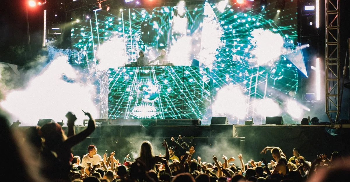 Vibrant music concert with DJ and crowd at night, showcasing lively atmosphere and dazzling lights.