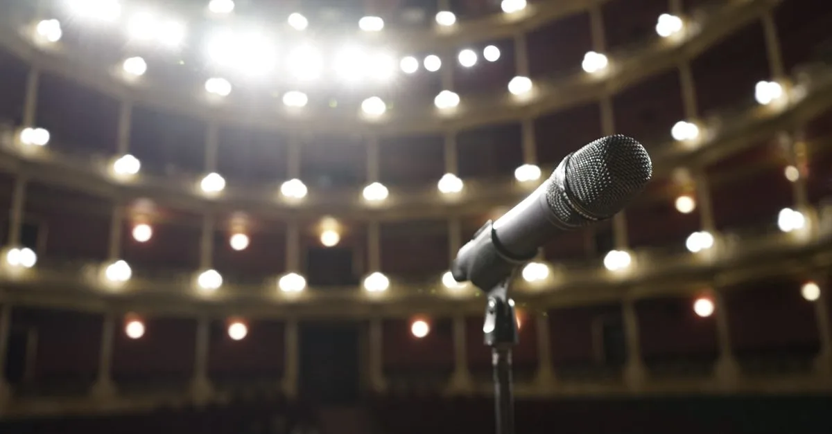 Close-up of a microphone on stage with bright theater lights in the background.