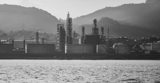 A monochrome shot of an industrial refinery near mountains, highlighting its structures.