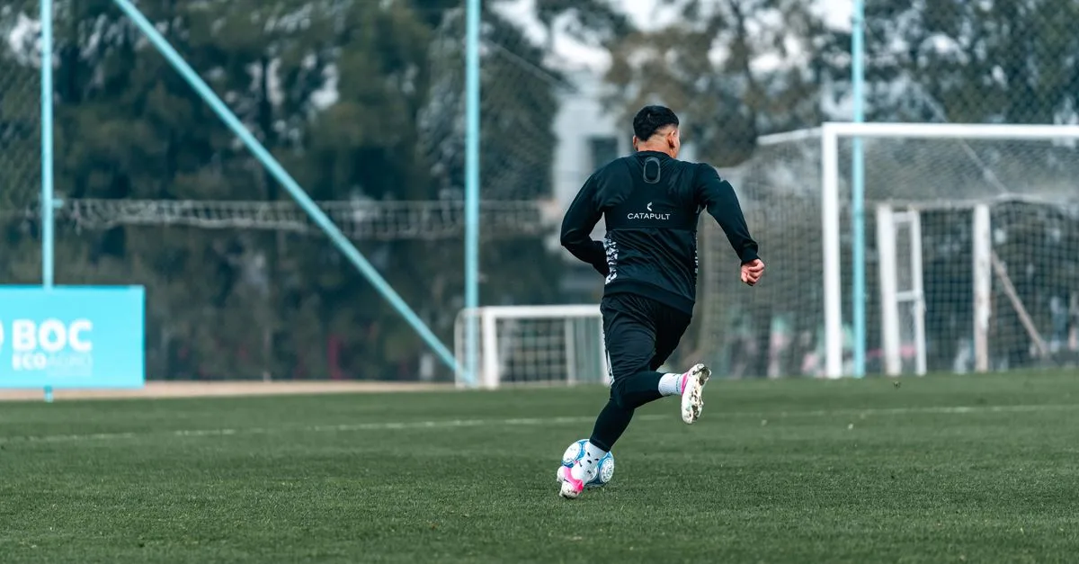 Football player practices dribbling on a professional outdoor field, emphasizing athleticism and skill.