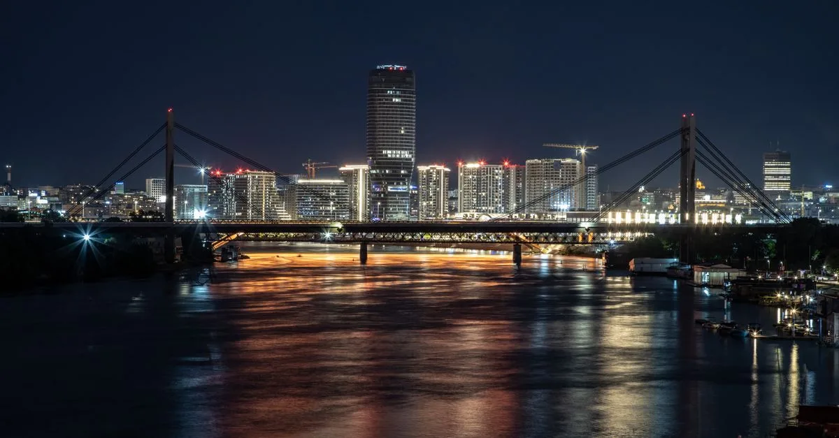 Explore this stunning cityscape featuring an illuminated bridge and skyscrapers reflecting on a tranquil river at night.