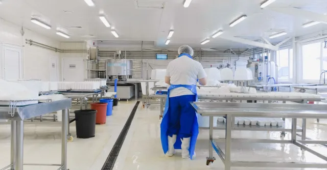 A person wearing protective clothing working in a bright, sterile laboratory environment.