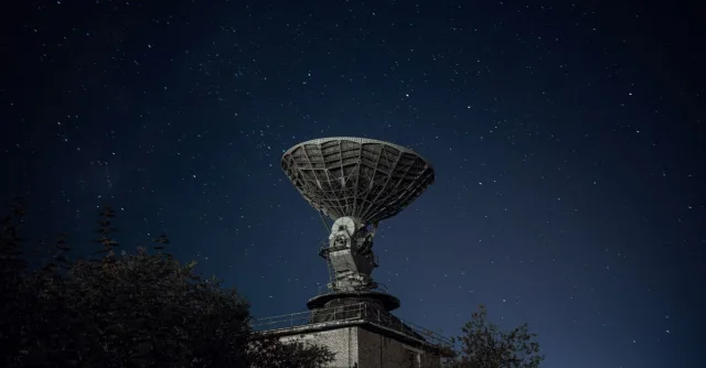 Radio telescope and green lush trees under blue sky with stars at night