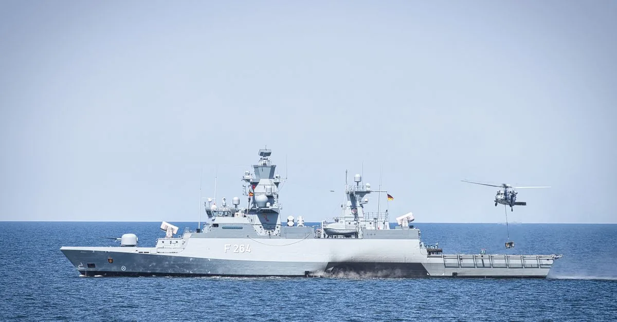 A naval frigate navigates open waters with a hovering helicopter, showcasing maritime operations.