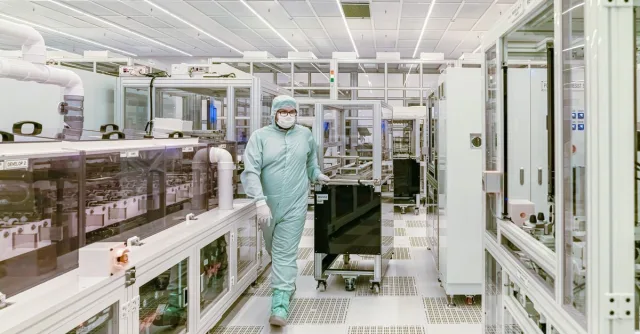 Scientist in protective gear walking in a high-tech cleanroom laboratory environment.