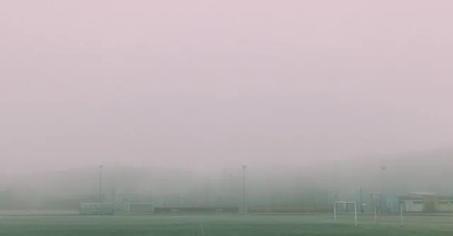 A foggy football field with goals visible, creating a serene and moody winter atmosphere.