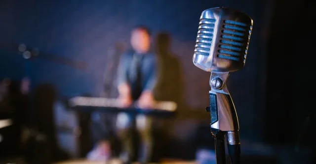 Close-up of a vintage microphone with a musician playing keyboard in the background, creating a musical atmosphere.