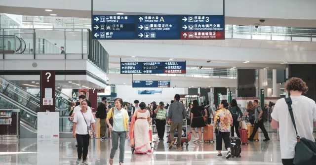 Crowded Hong Kong airport terminal with diverse passengers and informative signage.