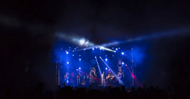 High-energy band performance on a stage with colorful lights and an engaged crowd.