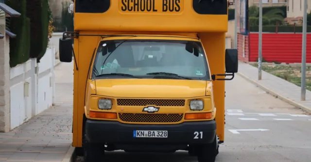 Front view of a yellow school bus parked along a quiet urban street. Street view