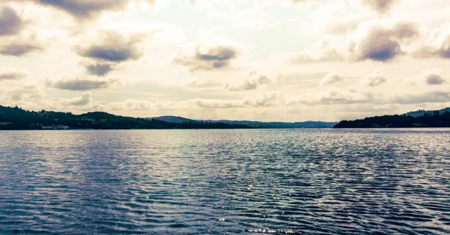 Peaceful Lake Windermere scene with calm waters and dramatic clouds in the scenic Lake District, England.
