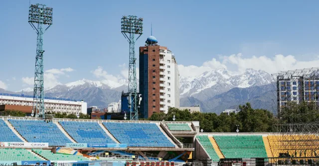 A striking view of a stadium in Almaty with snow-capped mountains in the background.