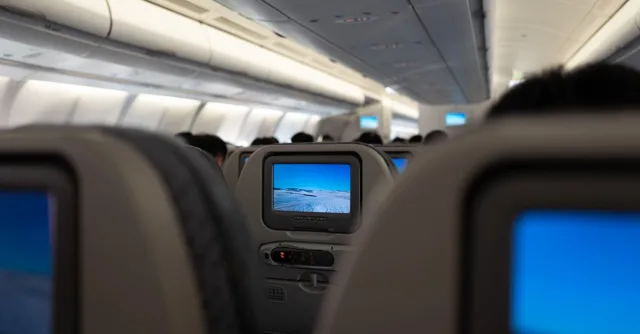 Interior of an airplane displaying in-flight entertainment screens and passenger seats.