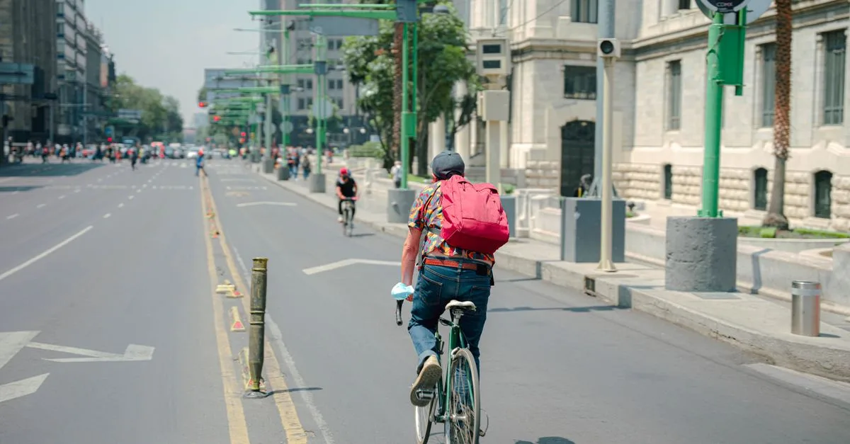 Back view of a man cycling on an empty city street on a sunny day.