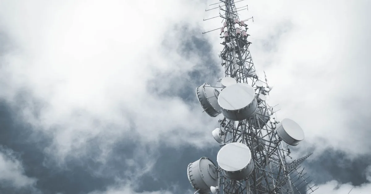 A towering communication mast with satellite dishes, set against a cloudy sky.