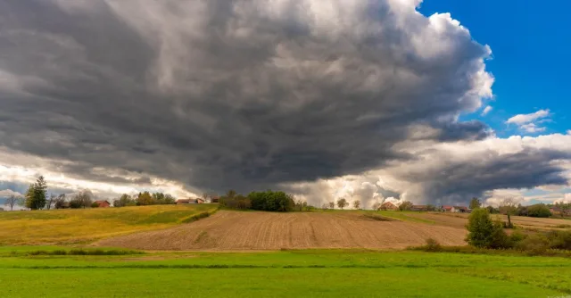 A picturesque rural landscape with dramatic storm clouds gathering over green fields and farmland.