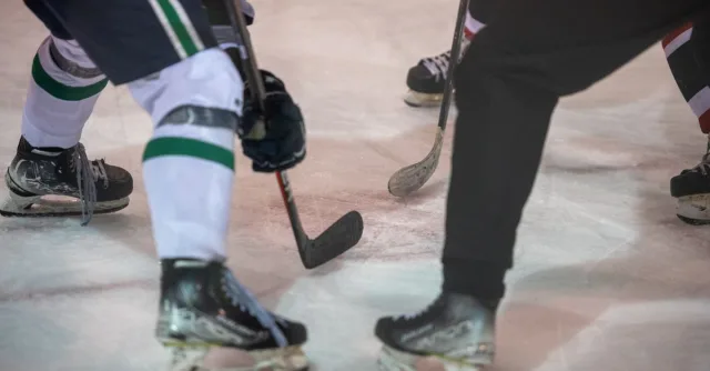 Close-up shot of ice hockey players in an intense face-off, showing skates and sticks on the ice.