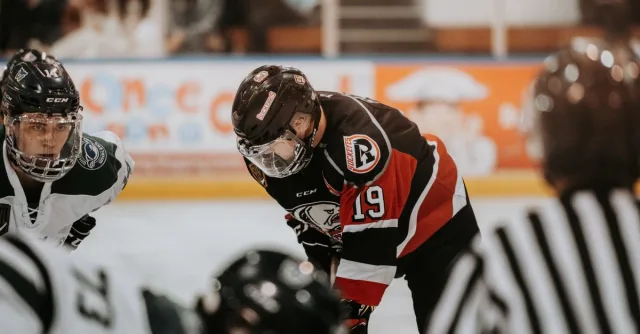Close-up action scene of ice hockey players in full gear competing on an indoor rink.