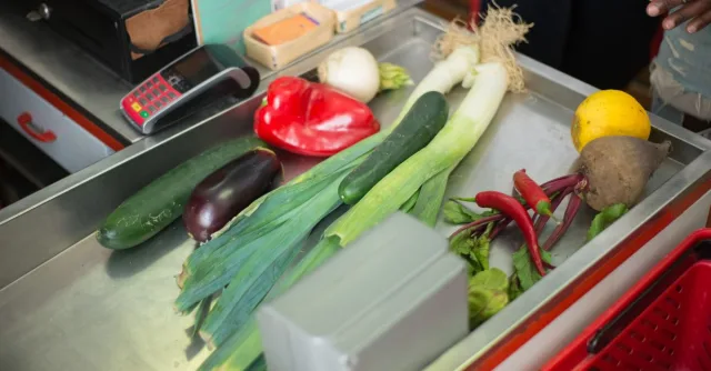 A selection of fresh vegetables on a stainless steel grocery checkout counter.