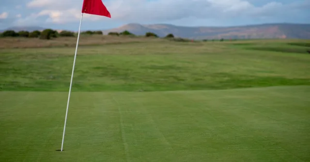 A beautiful golf course with a red flag on the green during a clear day.